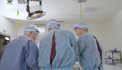 三个穿着医用工作服的人站在手术台上. 